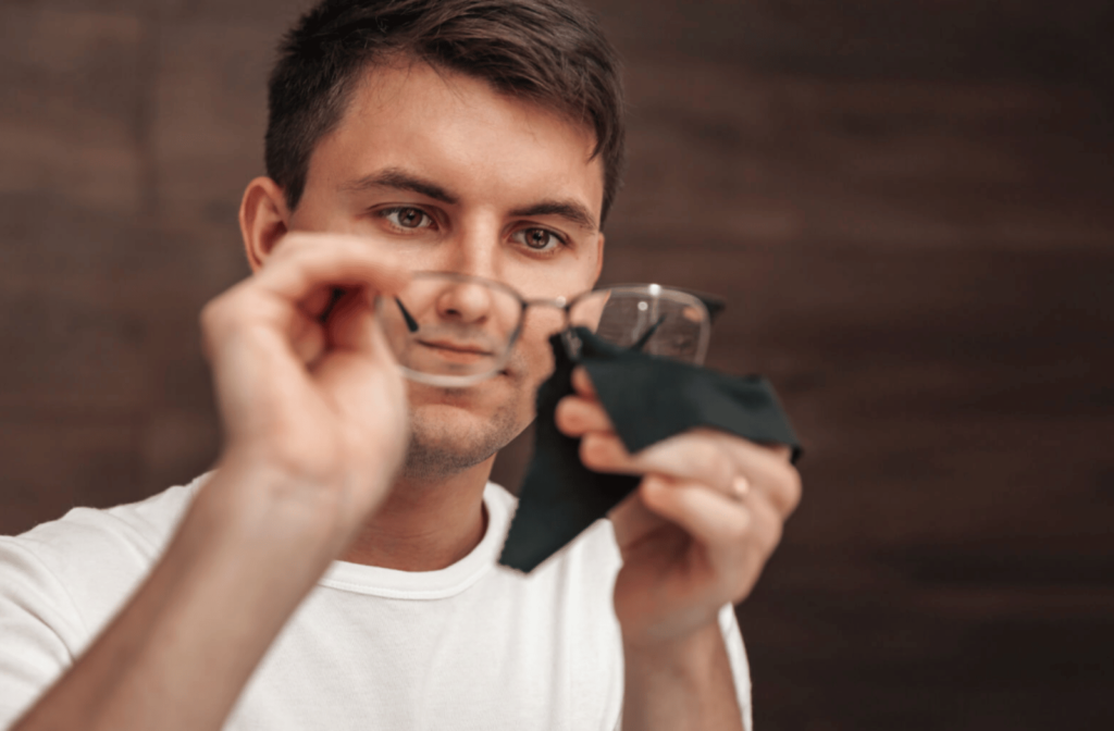 A man in a white shirt cleaning his glasses with a cleaning cloth