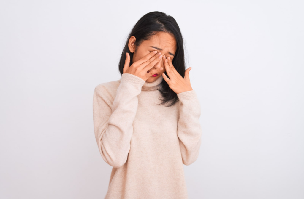 A young woman in a sweater is rubbing her eyes with both hands