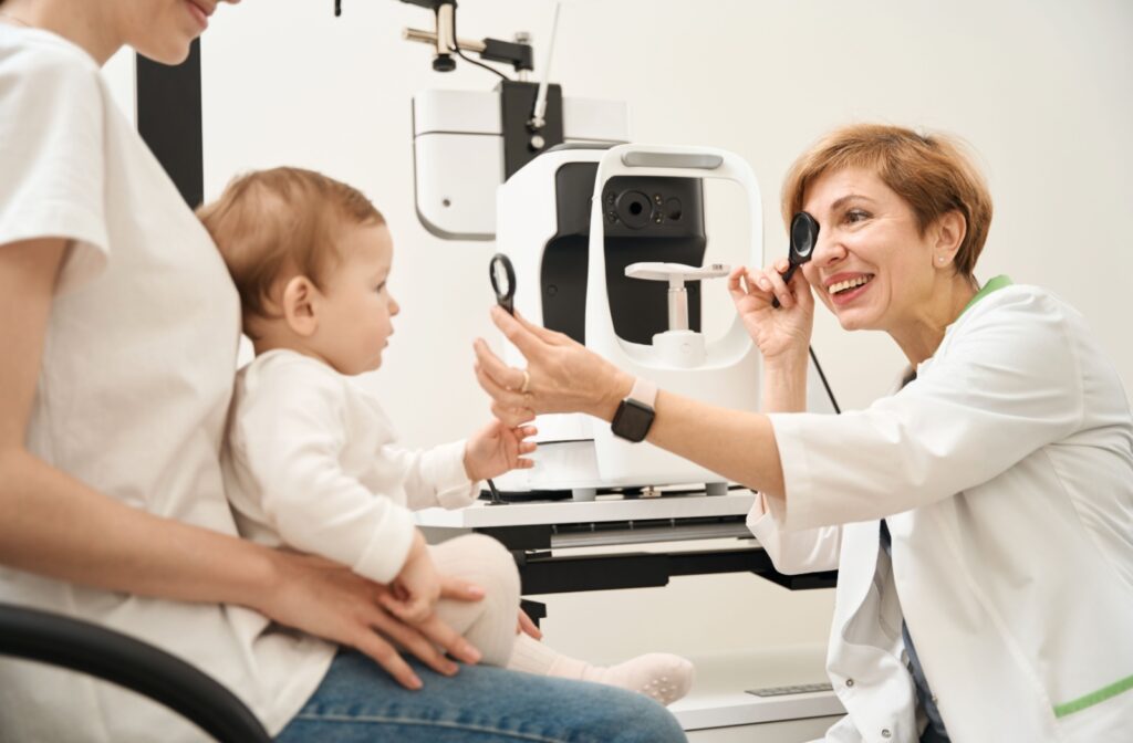 A baby on their parent's lap during their first eye exam while an optometrist smiles and tries to find the reason they're rubbing their eyes.