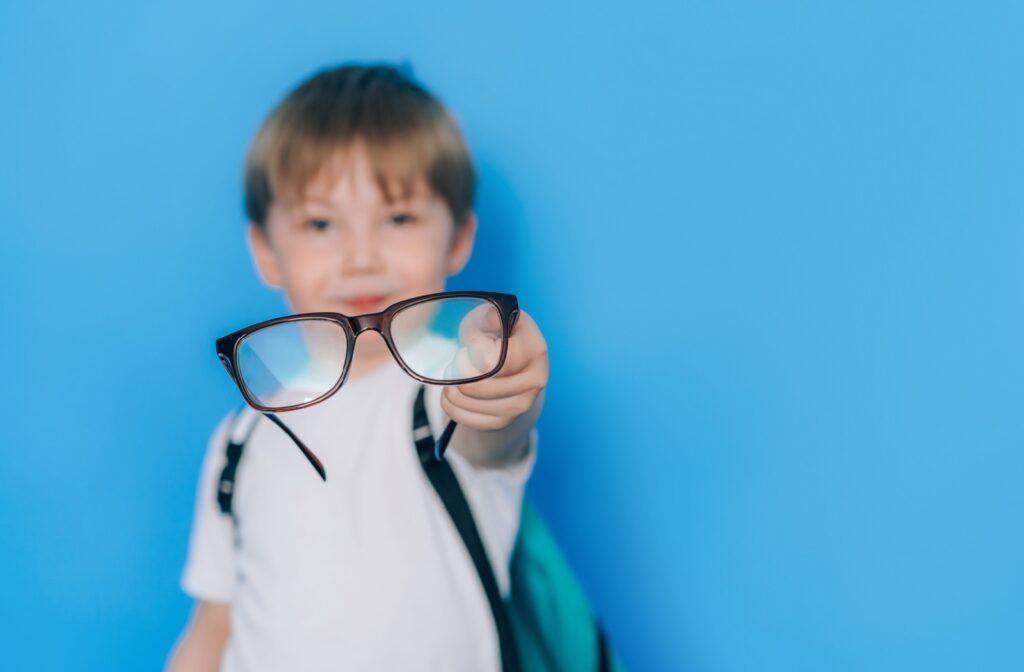 A young boy holding up a pair of glasses for myopia control.