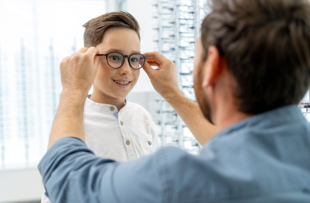 Person helping child try on new glasses in an eyewear store with display of frames in the background