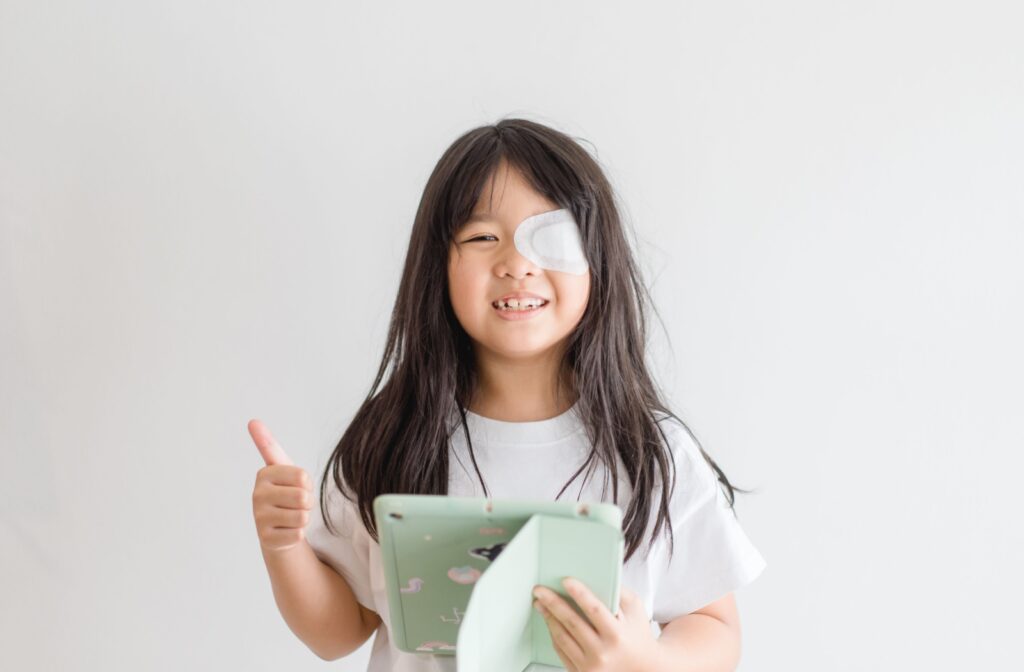 Young girl with long black hair and an eye patch holding an iPad with a thumbs up.