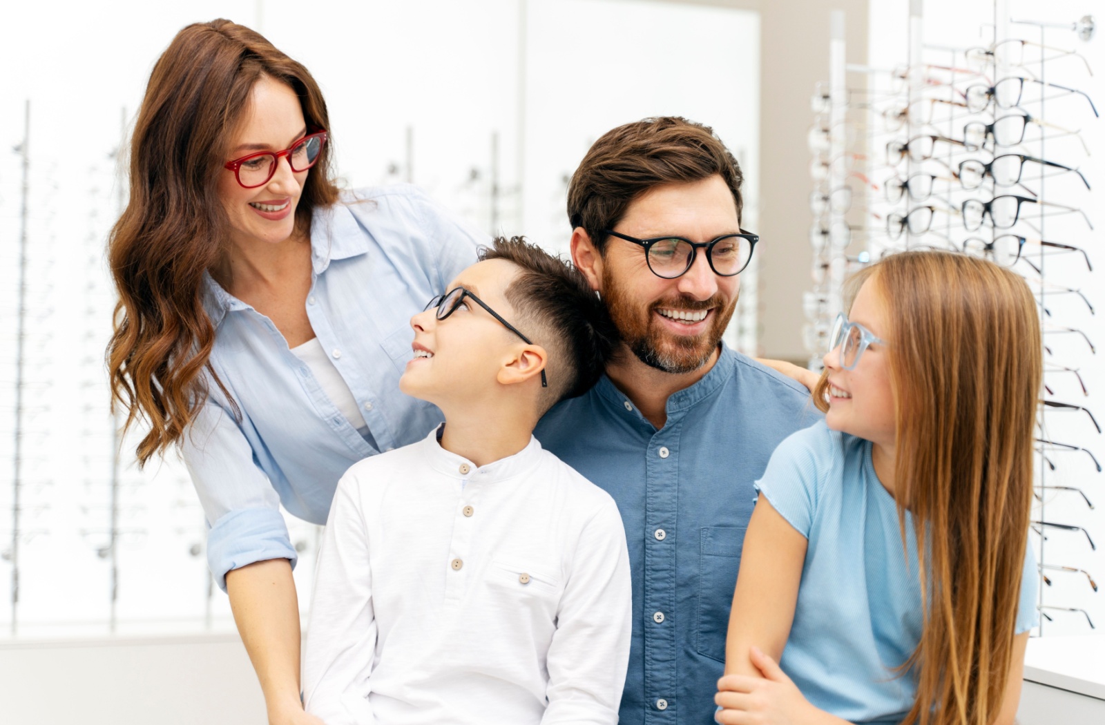 A family wearing glasses, sitting in front of a variety of frames at an optometry office.