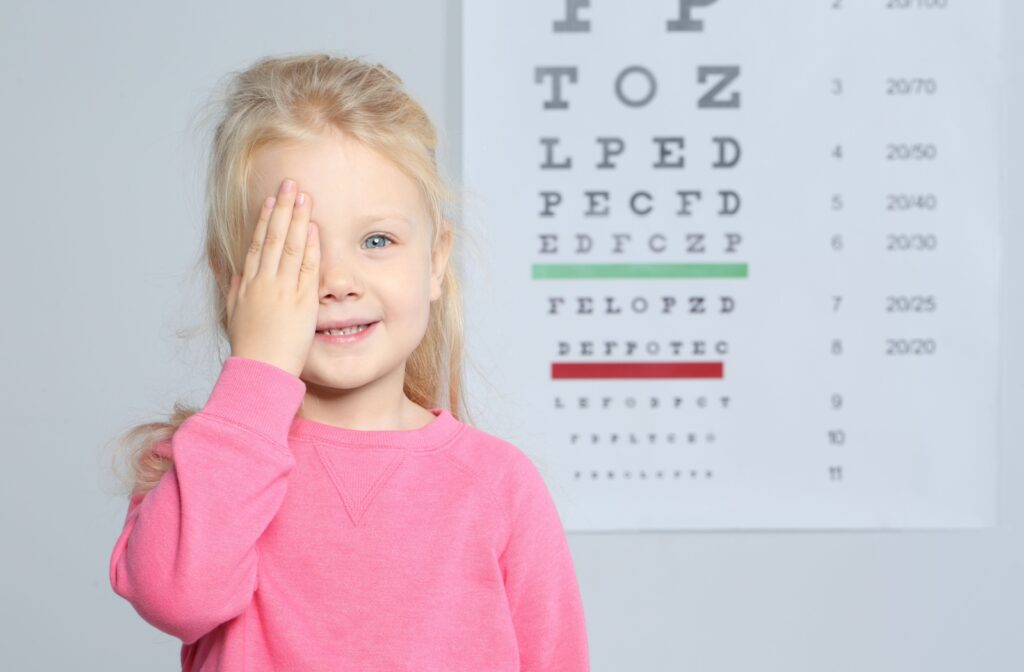 A young child at the eye doctor's office, covering one eye while looking at an eye chart.