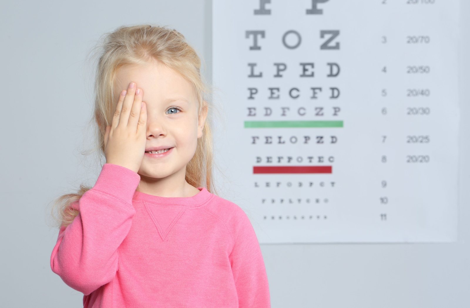 A young eye care patient covering one eye and reading an eye chart, having their eyes tested for signs of myopia.