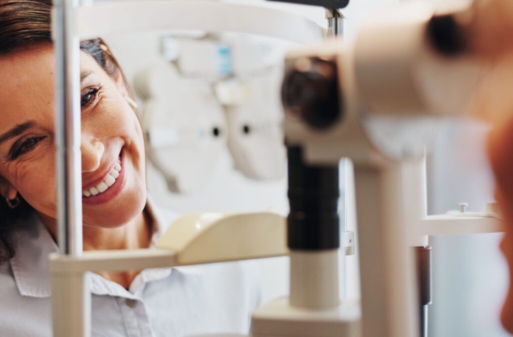 Optometrist smiling while performing an eye exam for a patient using vision testing equipment.