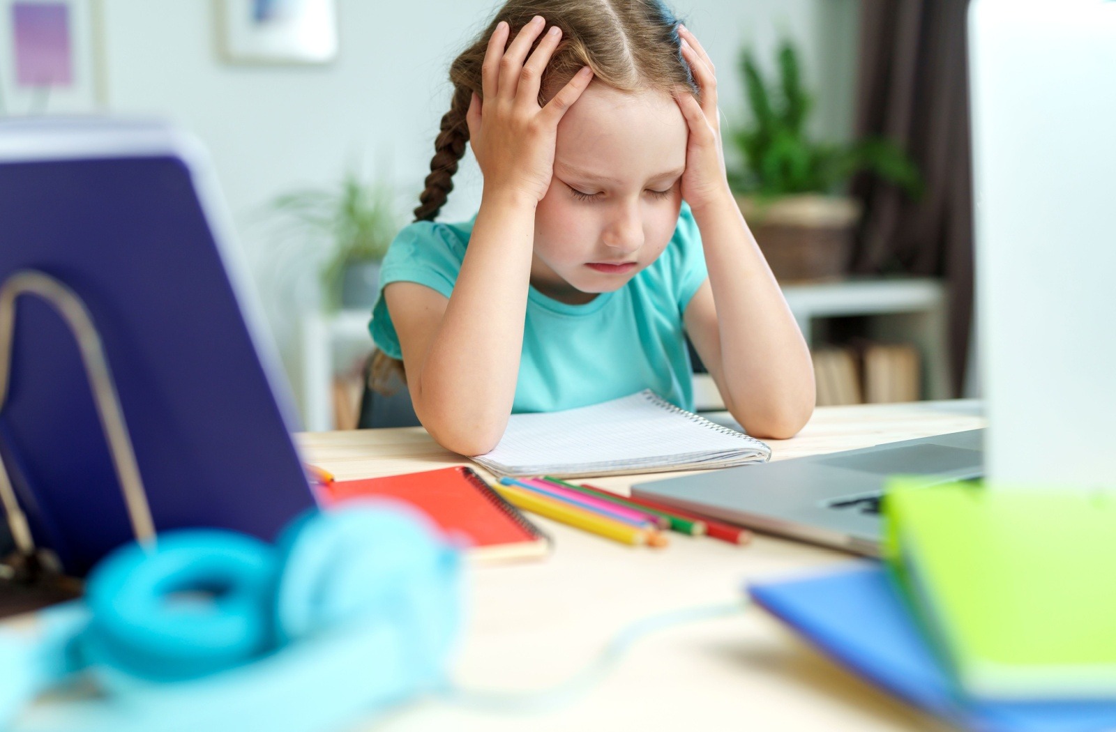 Child holding her head while studying at a desk, suggesting difficulty with focus, attention, or vision-related discomfort.